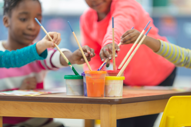 elementary students dipping paintbrushes into paint